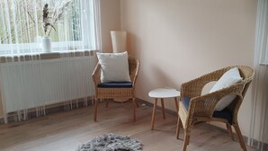 A room with two wicker chairs, one with a white cushion and another with a blue cushion, a small white table, and a white radiator. - Vacation near Oldenburg and North Lake, garden, children, beach club, water skiing, golf (Rastede)
