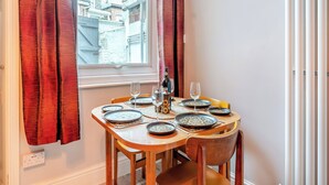 A dining table set with plates, glasses, and a bottle, positioned near a window with red curtains. - This ground floor apartment is less than a 10-minute walk away from the beach. (Scarborough)