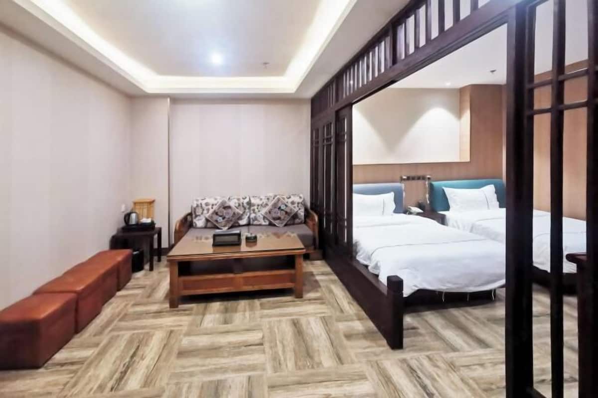 Ein Hotelzimmer mit Holzboden, einer Couch, einem Bett mit weißer Bettwäsche, einem Nachttisch und einer Holzwand.