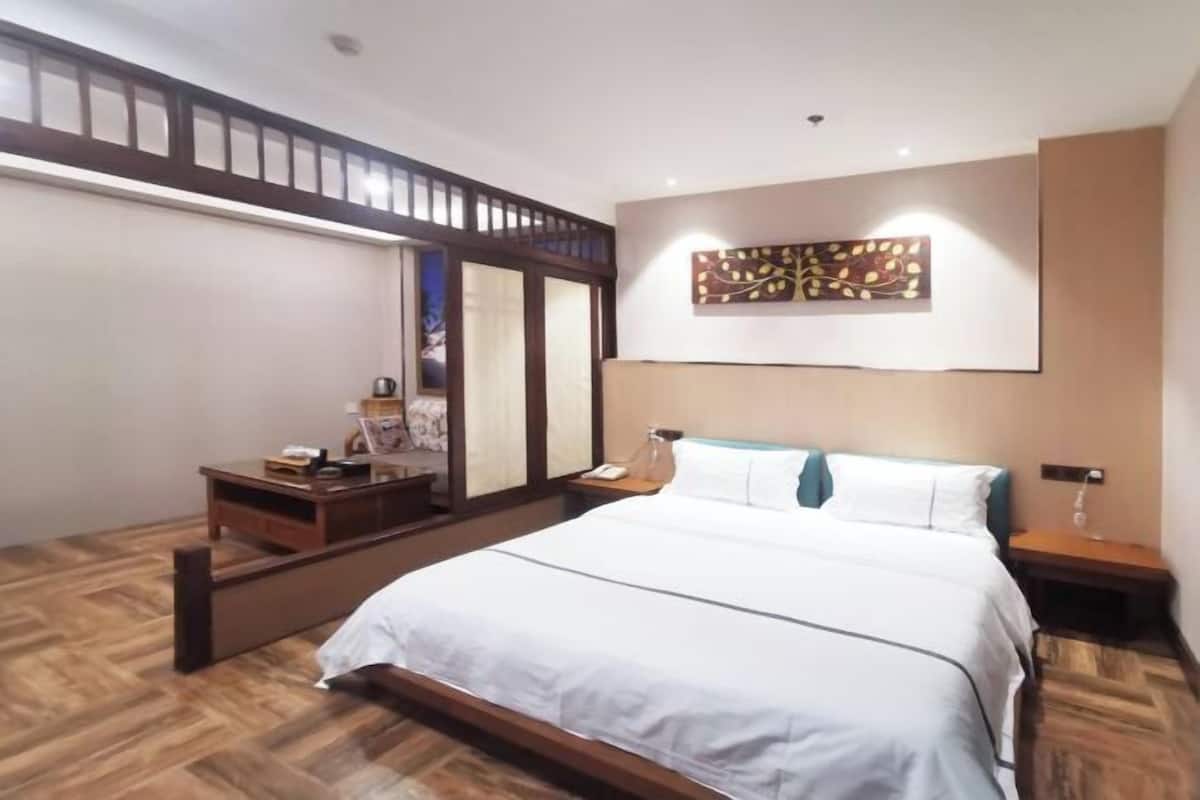 Ein Hotelzimmer mit einem großen Bett, Holzboden, einem Schreibtisch mit Lampe, einem Nachttisch und einem Wandbild.