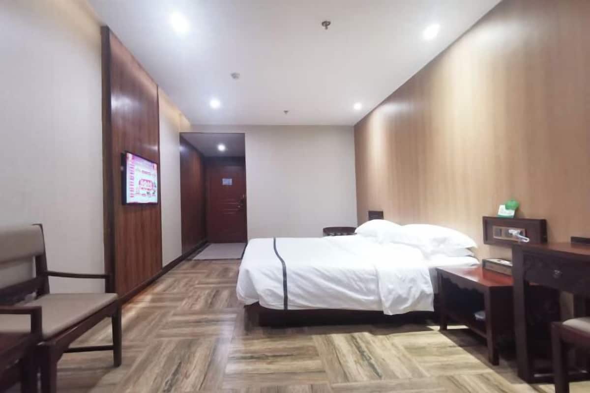 Ein Hotelzimmer mit einem Bett, einem Schreibtisch, einem Sessel und einem Fernseher an der Wand.
