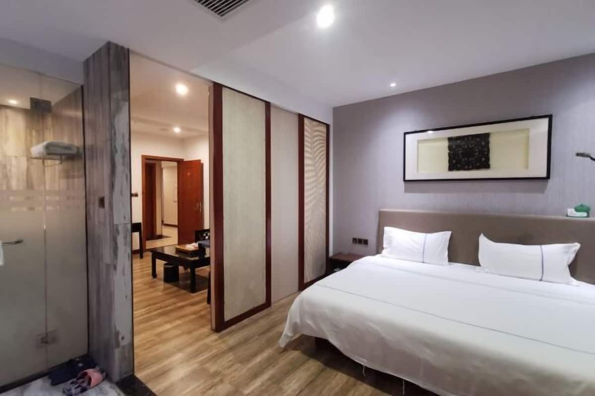 Ein Hotelzimmer mit einem großen Bett, Holzboden, einer Schiebetür und einem gerahmten Bild an der Wand.