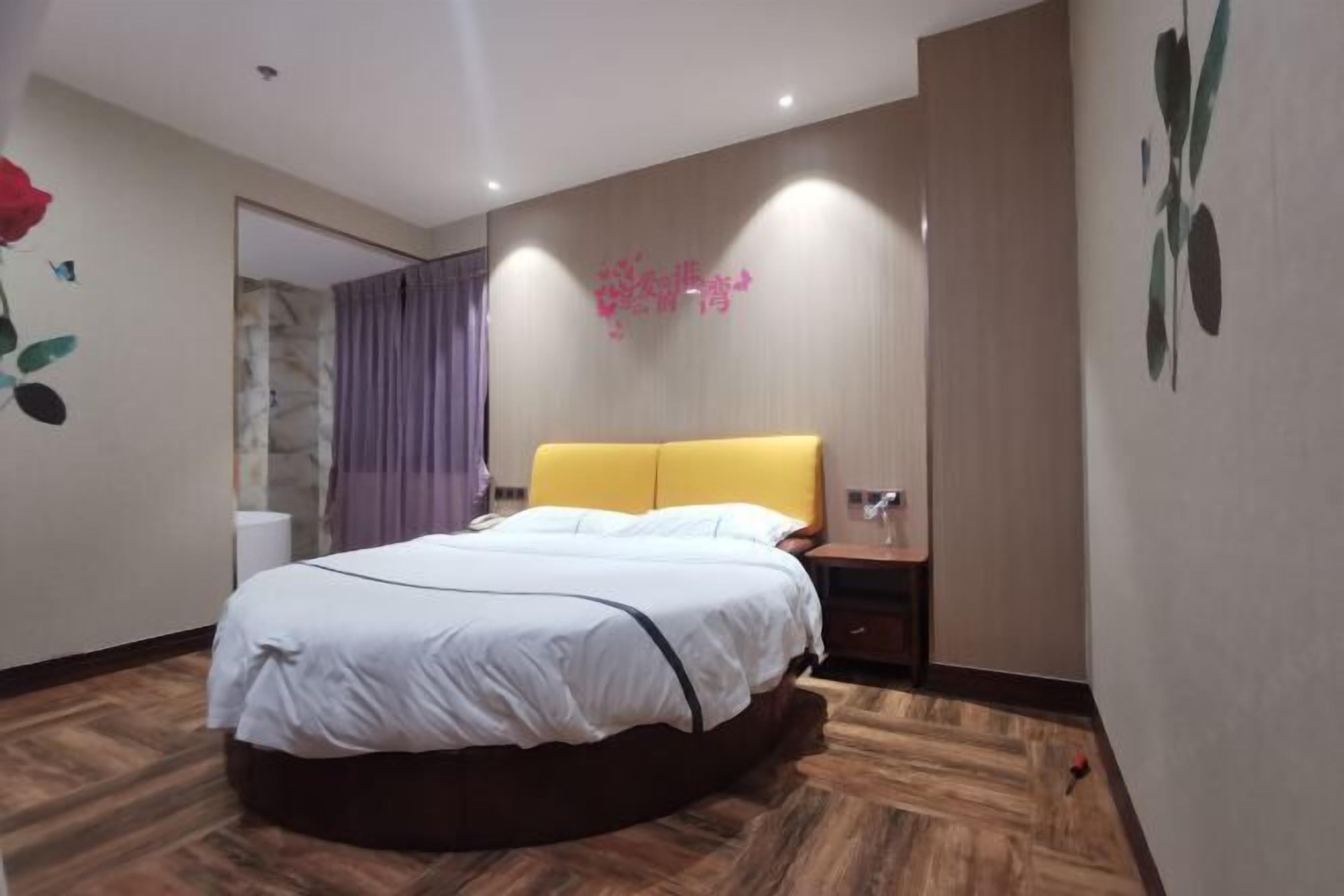 A modern bedroom with a bed, a nightstand, a wall-mounted shelf, and a bathroom visible through a glass door.