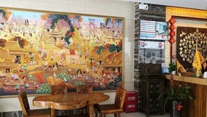 A dining area with a large mural depicting a traditional scene, wooden furniture, and a reception desk with a decorative plant. - Feicui Boutique Hotel (Jinjiang)