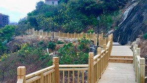 A wooden boardwalk with railings, surrounded by greenery and a rocky landscape. - Feicui Boutique Hotel (Jinjiang)