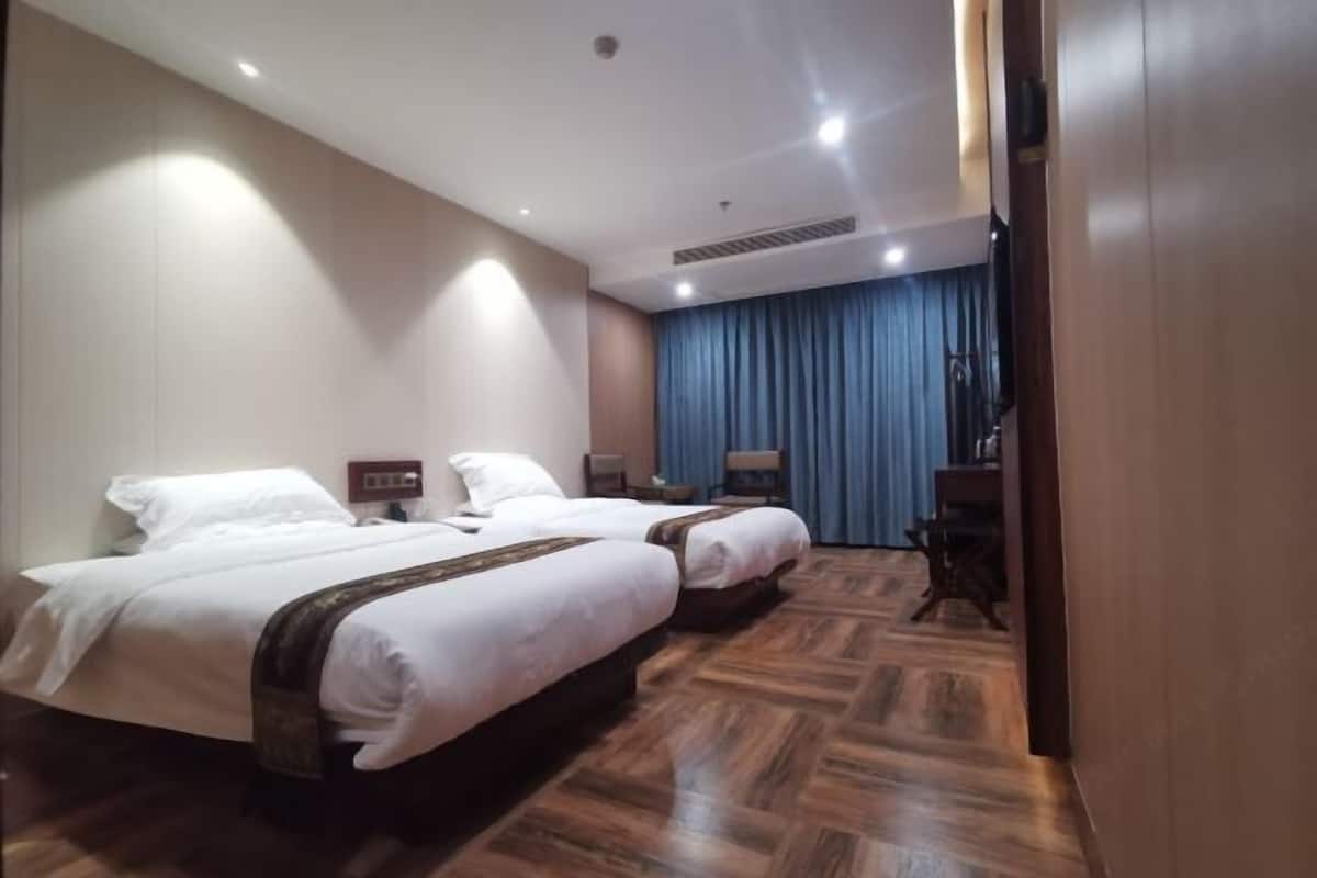 Ein Hotelzimmer mit zwei Betten, einem Schreibtisch, einem Stuhl und einem blauen Vorhang.