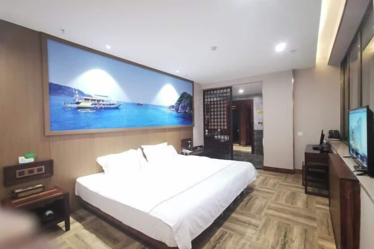 Ein Hotelzimmer mit einem großen Bett, einem Fernseher und einem Wandbild mit einer Küstenlandschaft.