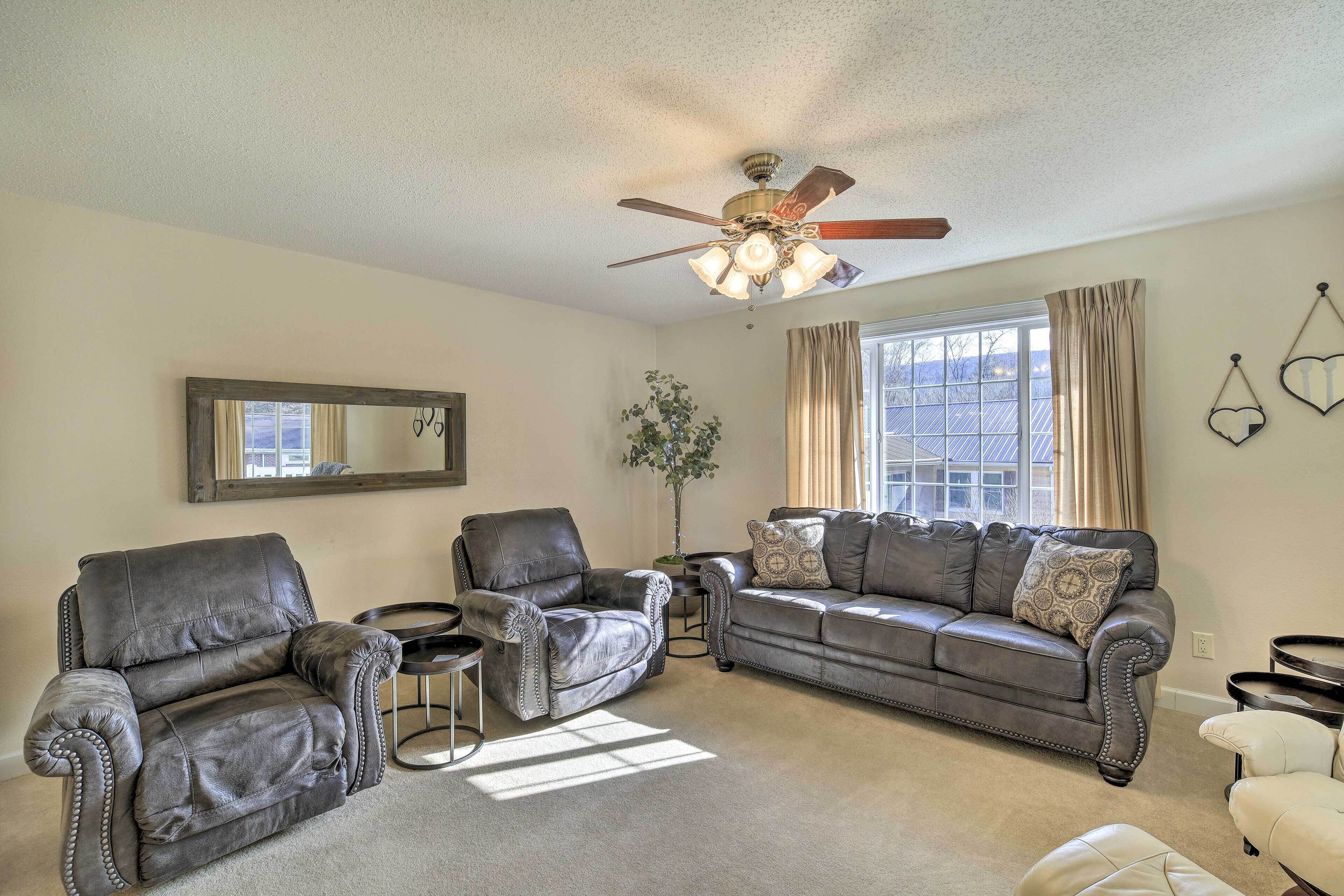 A living room with a ceiling fan, a sofa, two armchairs, a small side table, and a potted plant.