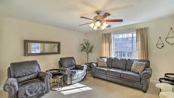 A living room with a ceiling fan, a sofa, two armchairs, a small side table, and a potted plant.