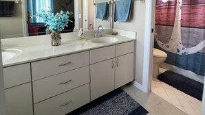 Un bagno con doppio lavabo, uno specchio grande, un portasciuga e una tenda da doccia con decorazioni a tema nautico.