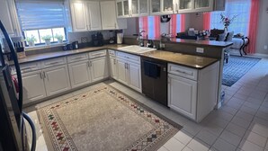 Un'ampia cucina con mobili bianchi, una grande isola, un ventilatore a soffitto e una finestra con persiane.