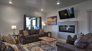 A living room with a brown leather sofa, a wooden coffee table, a patterned rug, a television, and a fireplace.