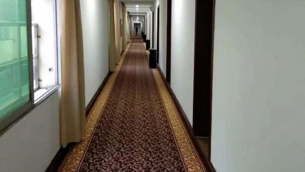 A long, narrow hallway with a patterned carpet and white walls. - Shujie Hotel (Ji'an)