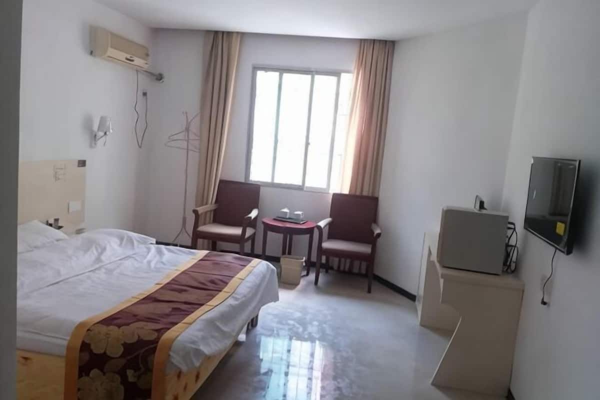 A hotel room with a bed, two armchairs, a small table, a TV, and a desk with a computer.