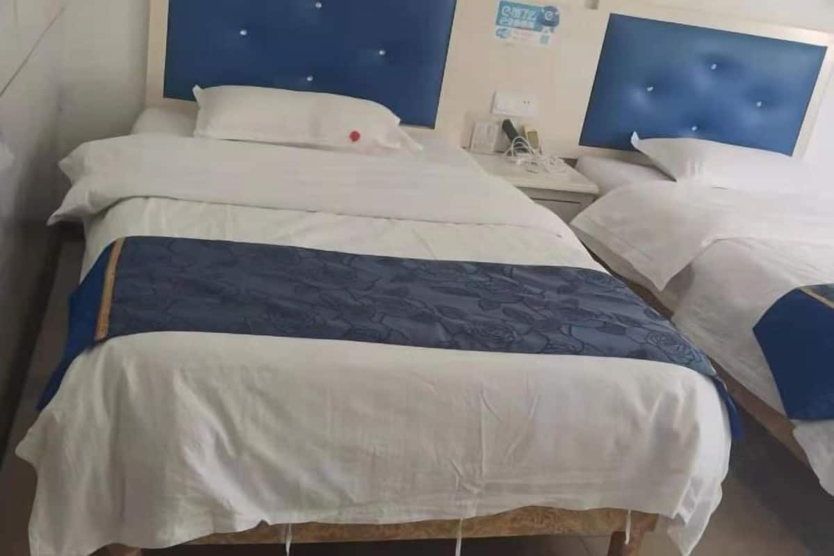 A hotel room with two beds, each with a blue headboard, white bedding, and a small bedside table with a phone and charger.