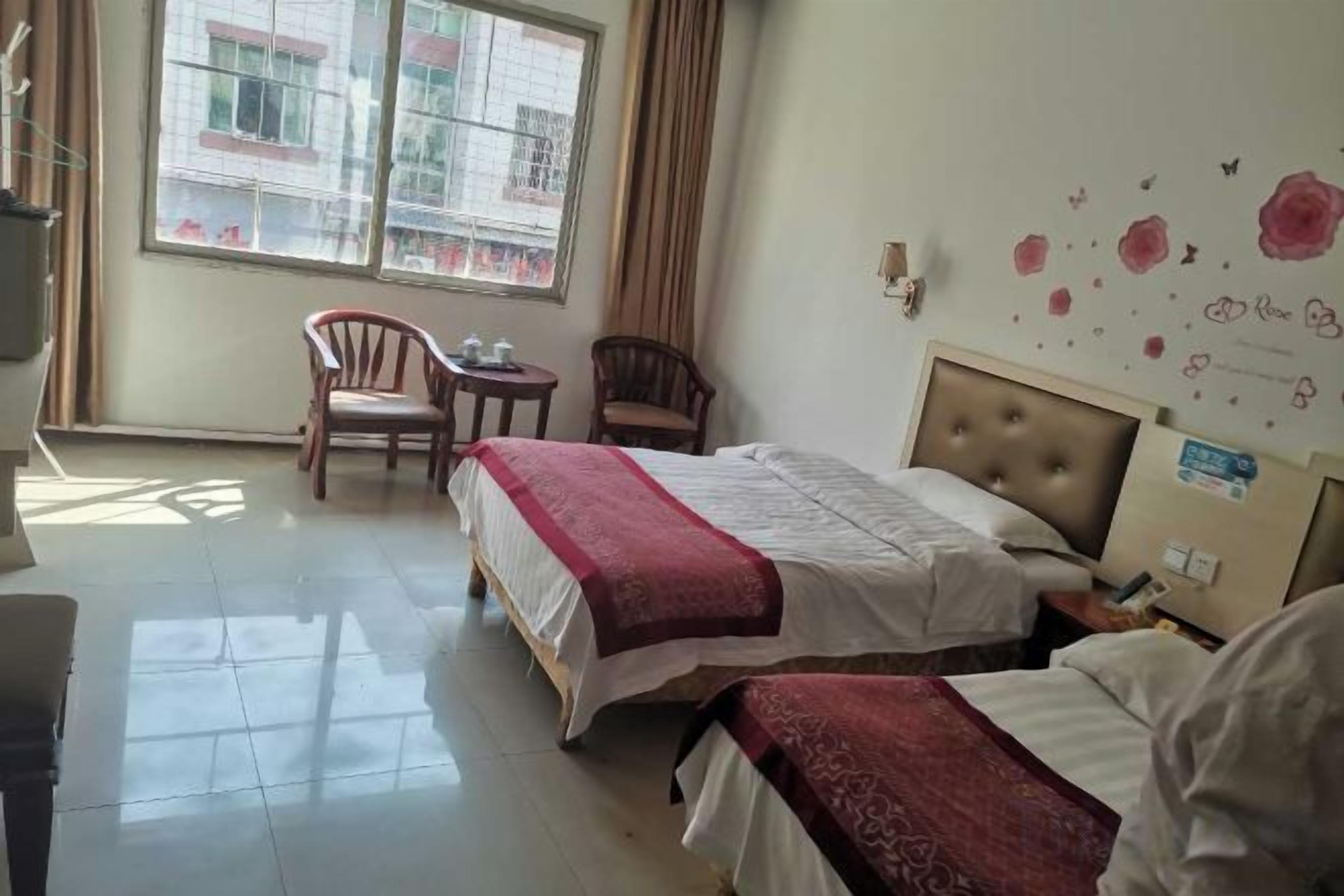 A hotel room with two beds, a small table, two chairs, and a window with curtains.