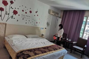 A hotel room with a bed, a chair, a desk, and a wall with floral decals. - Shujie Hotel (Ji'an)