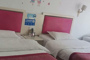 A hotel room with two beds, a nightstand with a phone and a coffee maker, and a wall-mounted lamp.