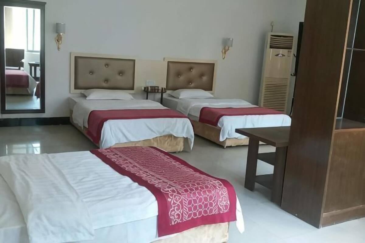 A hotel room with two beds, a wooden table, a mirror, and a wardrobe.