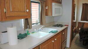 A compact kitchen with wooden cabinets, a white sink, a microwave, and a stove. - Gwin's Lodge Poplar Chalet #2 (Cooper Landing)