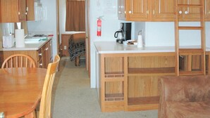 A compact kitchen with wooden cabinets, a dining table, and a loft bedroom with a bunk bed. - Gwin's Lodge Poplar Chalet #2 (Cooper Landing)