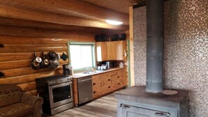 L’intérieur d’un chalet rustique est doté d’un poêle à bois, d’une petite cuisine avec un évier et des placards, ainsi que d’un canapé à motifs.
