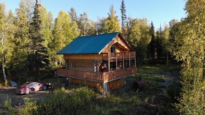 Une cabane avec une façade en bois, un balcon et une voiture garée à proximité.
