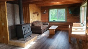 L’intérieur d’un chalet accueillant, avec un poêle à bois, un canapé, une table et une fenêtre donnant sur le paysage extérieur.
