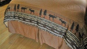 Tunnelmallinen huone, jossa on suuri sänky, kaksi pienempää sänkyä, puuseinät, Alaskan maisemaa esittävä taulu ja ikkuna, jossa on verhot.