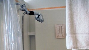 Une douche avec un rideau transparent, une pomme de douche à main et une serviette suspendue à un porte-serviettes.