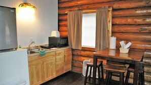 Una cocina funcional con refrigerador, lavaplatos y microondas. Hay una mesa de comedor de madera con sillas y una ventana con cortinas.