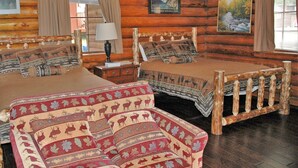 Una habitación tipo cabaña de madera con dos camas, un cabecero de madera y un sofá rojo con estampado.
