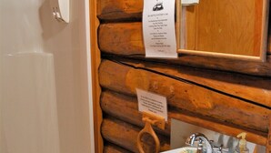 Une salle de bain avec un mur en rondins de bois, une baignoire blanche, un tabouret en bois et un lavabo avec un miroir au-dessus.
