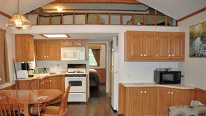 Uma cozinha compacta com armários de madeira, fogão, micro-ondas e um espaço de refeições com mesa e cadeiras.