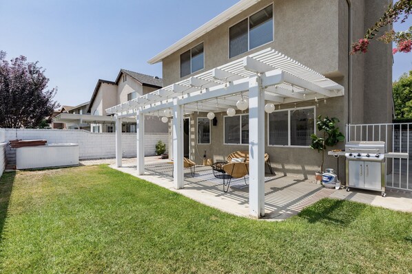 Un jardin avec un patio couvert, un barbecue extérieur et un espace détente.