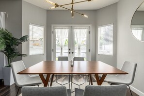 Une salle à manger moderne avec une table en bois, des chaises recouvertes d’un tissu gris et une plante en pot.