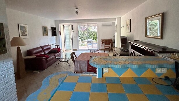 Una sala de estar con sofá, una mesa de centro y televisor. Hay un ventanal corredero que da a un balcón.