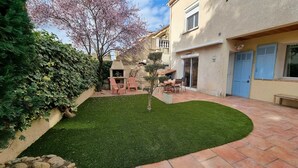 Un patio con un pequeño césped, mobiliario exterior y un edificio con una puerta azul.