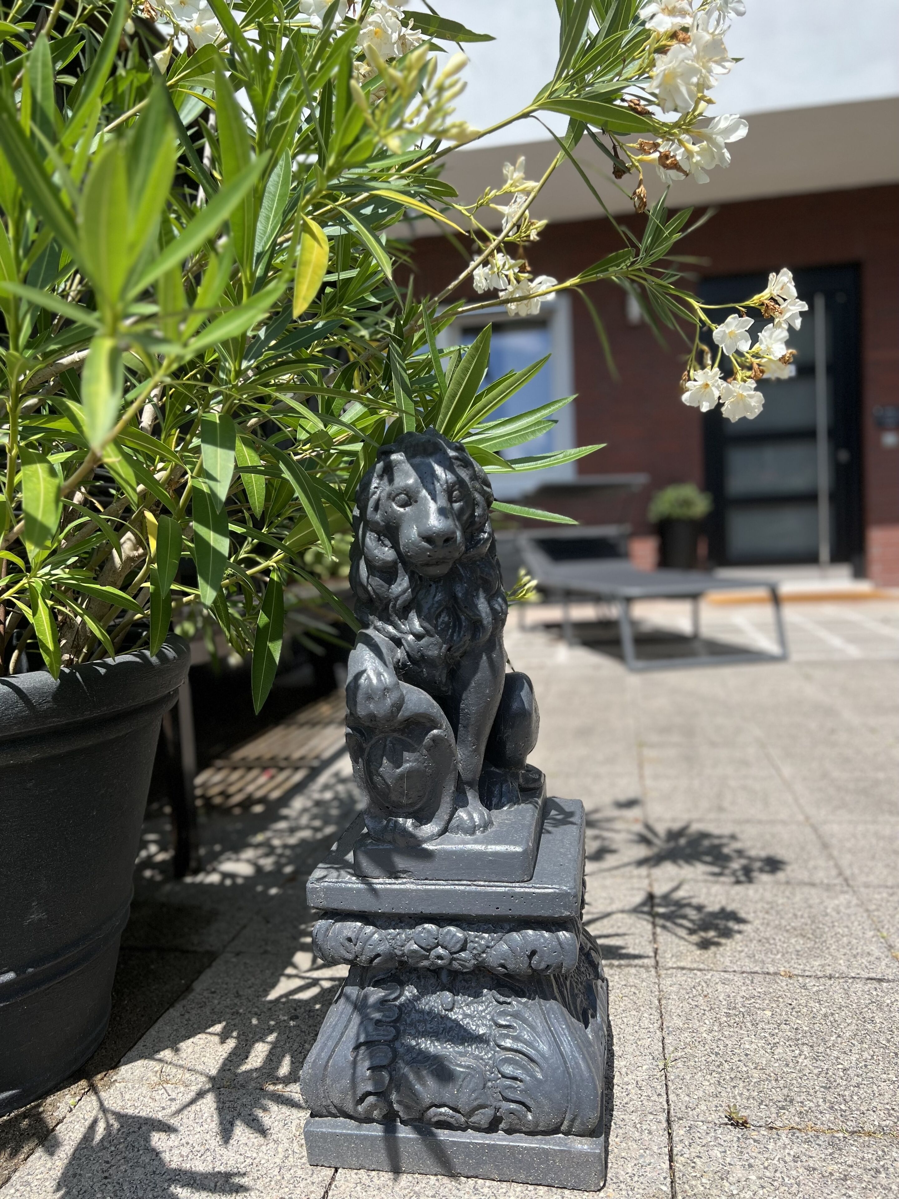 Une statue de lionne, placée dans un jardinière, avec un bâtiment et un banc en arrière-plan.