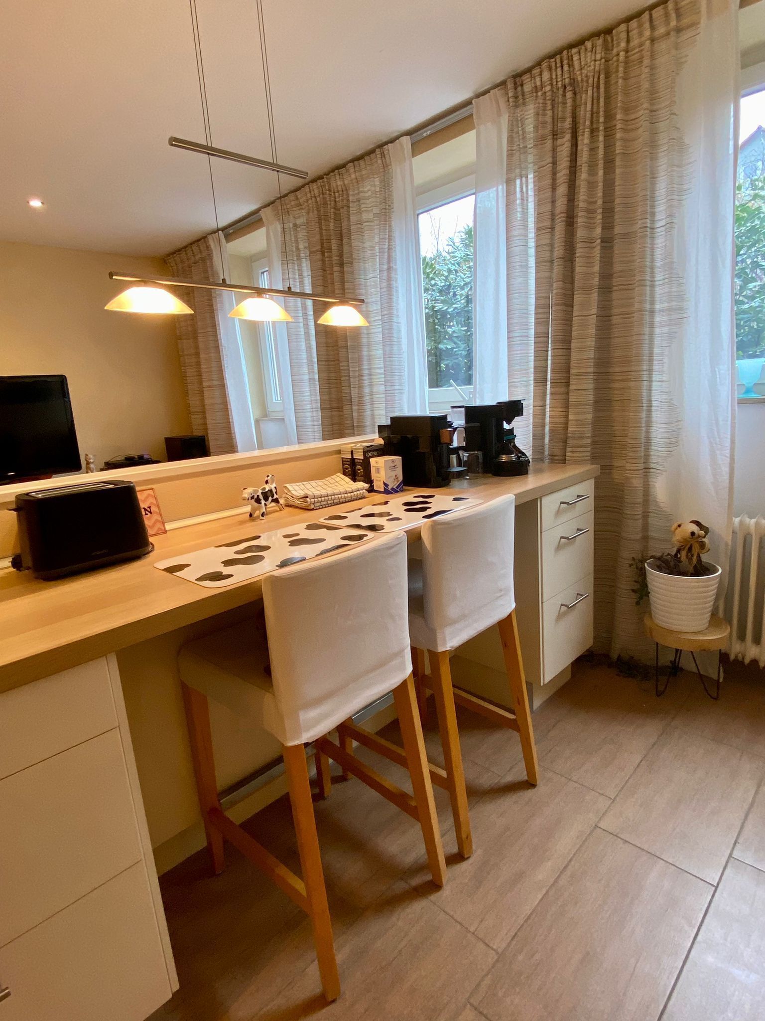 A modern kitchen with a wooden countertop, two bar stools, a coffee machine, and a small table with a teddy bear.