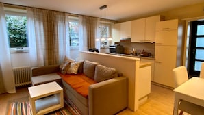 Un espacio habitable compacto con sofá, una pequeña mesa de comedor, zona de cocina y un radiador.