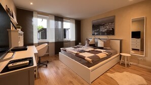 Un dormitorio moderno con cama, escritorio, silla y un ventanal amplio.