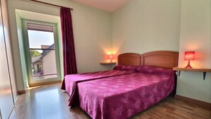 Habitación doble con dos camas, cabeceros de madera, suelo de madera, una ventana con cortinas y dos lámparas de noche.