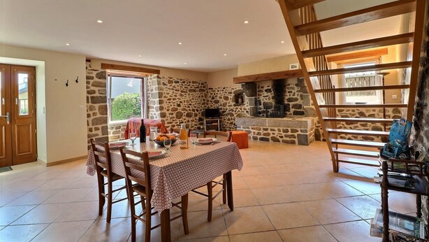 Un comedor con pared de piedra, una escalera de madera y una chimenea de piedra.