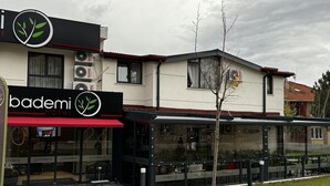 Un hotel con fachada moderna, ventanas grandes y un espacio exterior con mesas.
