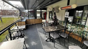 Un área de comedor al aire libre con cerramiento de vidrio, una barra de madera y un árbol de Navidad.