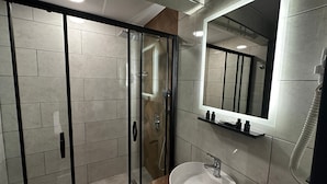 Un baño moderno con ducha envuelta en vidrio, un espejo grande y un lavamanos con grifo.