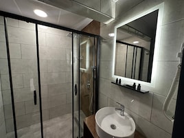 Un baño moderno con ducha envuelta en vidrio, un espejo grande y un lavamanos con grifo.