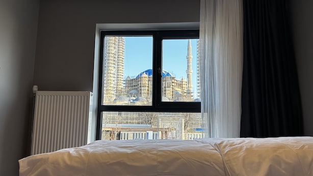 Habitación de hotel con un amplio ventanal que ofrece vistas de la ciudad, incluyendo un rascacielos con aguja.