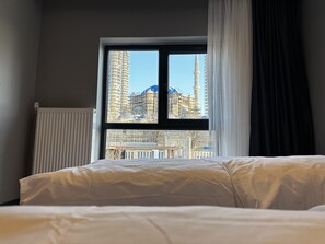 Een hotelkamer met een groot raam dat uitzicht biedt op een stadsbeeld, inclusief een hoog gebouw met een spits.